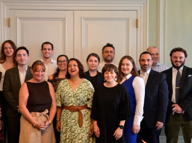 A group of approximately 14-15 professionals, including men and women, in formal attire, smiling and posed for a group portrait.