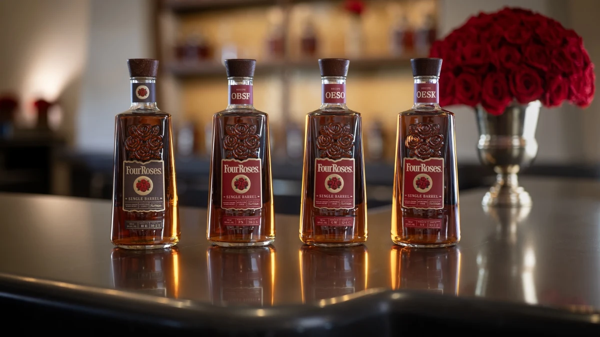 Four bottles of Four Roses Single Barrel bourbon arranged on a reflective surface with roses in background