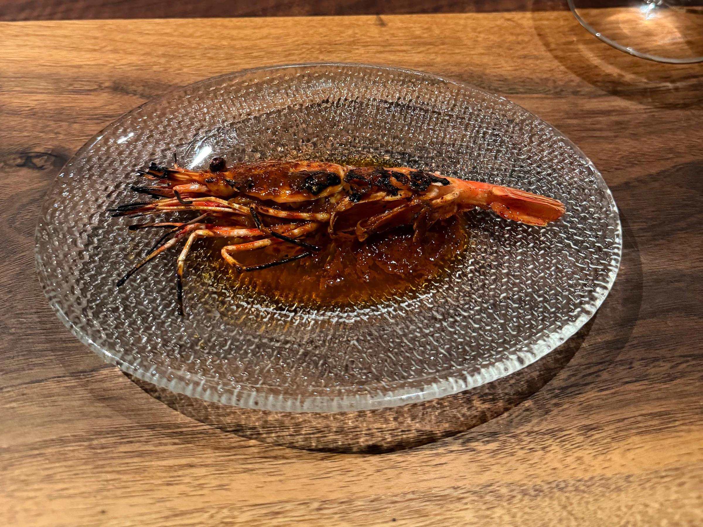 Whole prawn glazed and charred over Saison’s live-fire hearth, served on a clear glass plate
