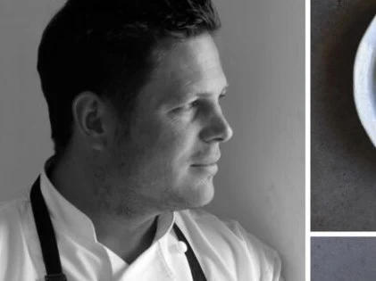 Black and white portrait photograph of a man wearing a white chef's coat, shown in profile against a gray background.
