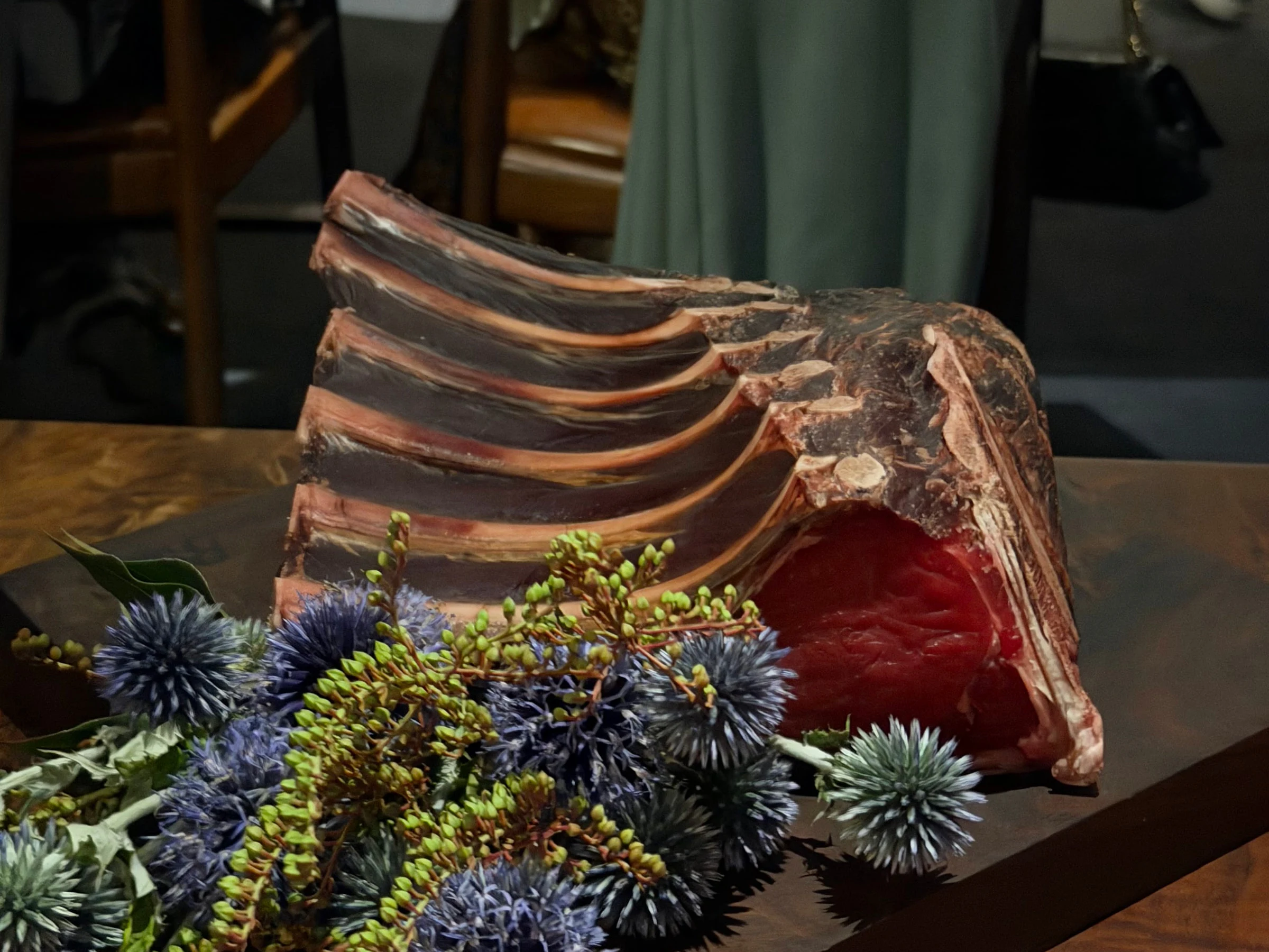 Whole rib presentation with long bones and fresh blue-green botanical garnishes at Saison