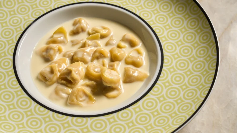 A bowl of Filipino lumpia (spring rolls) in a creamy sauce on a decorative yellow-patterned plate