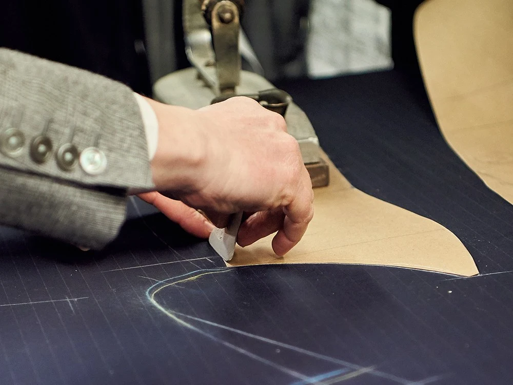 Hand tracing a paper pattern on dark fabric with a tailor's chalk.